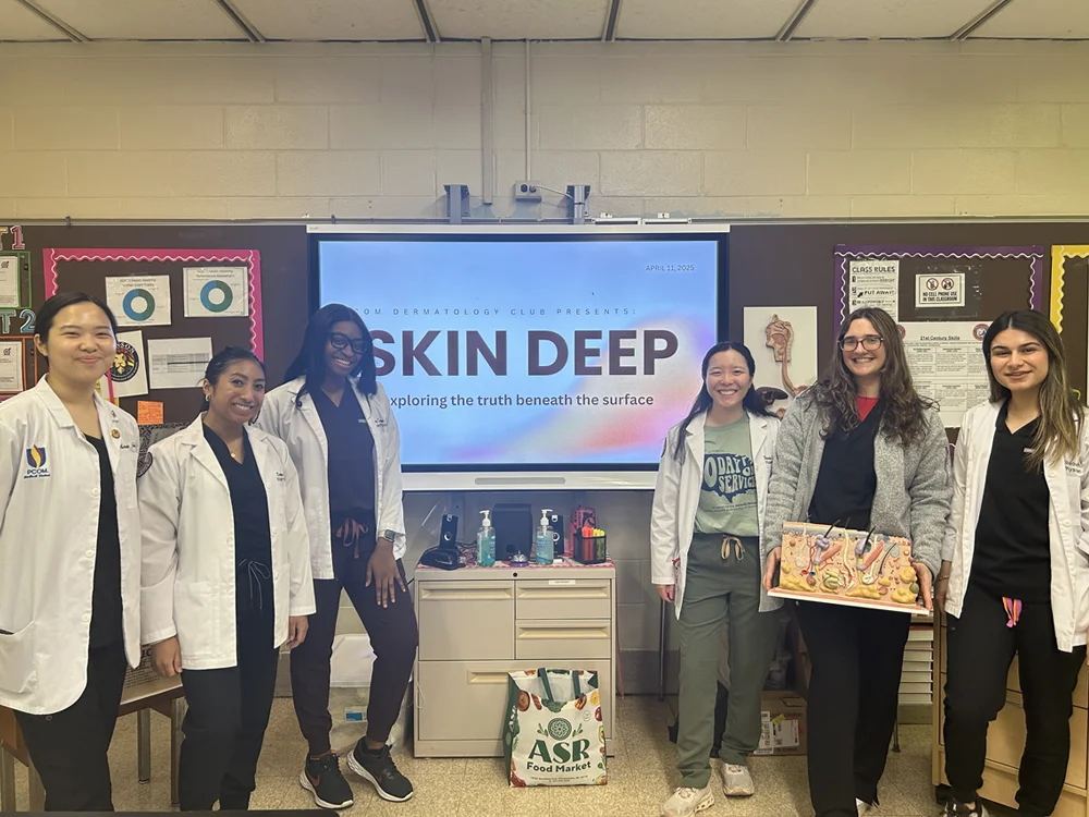 Medical students in white lab coats stand together in front of presentation screen