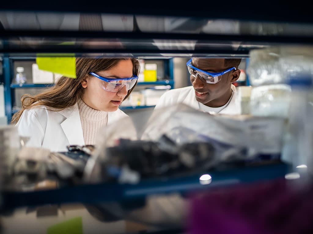 Two PCOM biomed students smile as they work in a laboratory